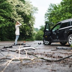 Young woman standing by the damaged car after a car accident.