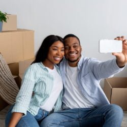 Relocation and ownership concept. Happy young black couple making selfie after moving to own house